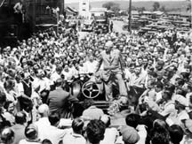 Historic photo of Endicott Johnson: Surrounded by workers from Endicott Johnson shoes, George F. Johnson sits on a car windshield as he talks with his employees, circa 1935. Copyright 1996 Binghamton Press & Sun-Bulletin. Photographer: Beth Kaplan